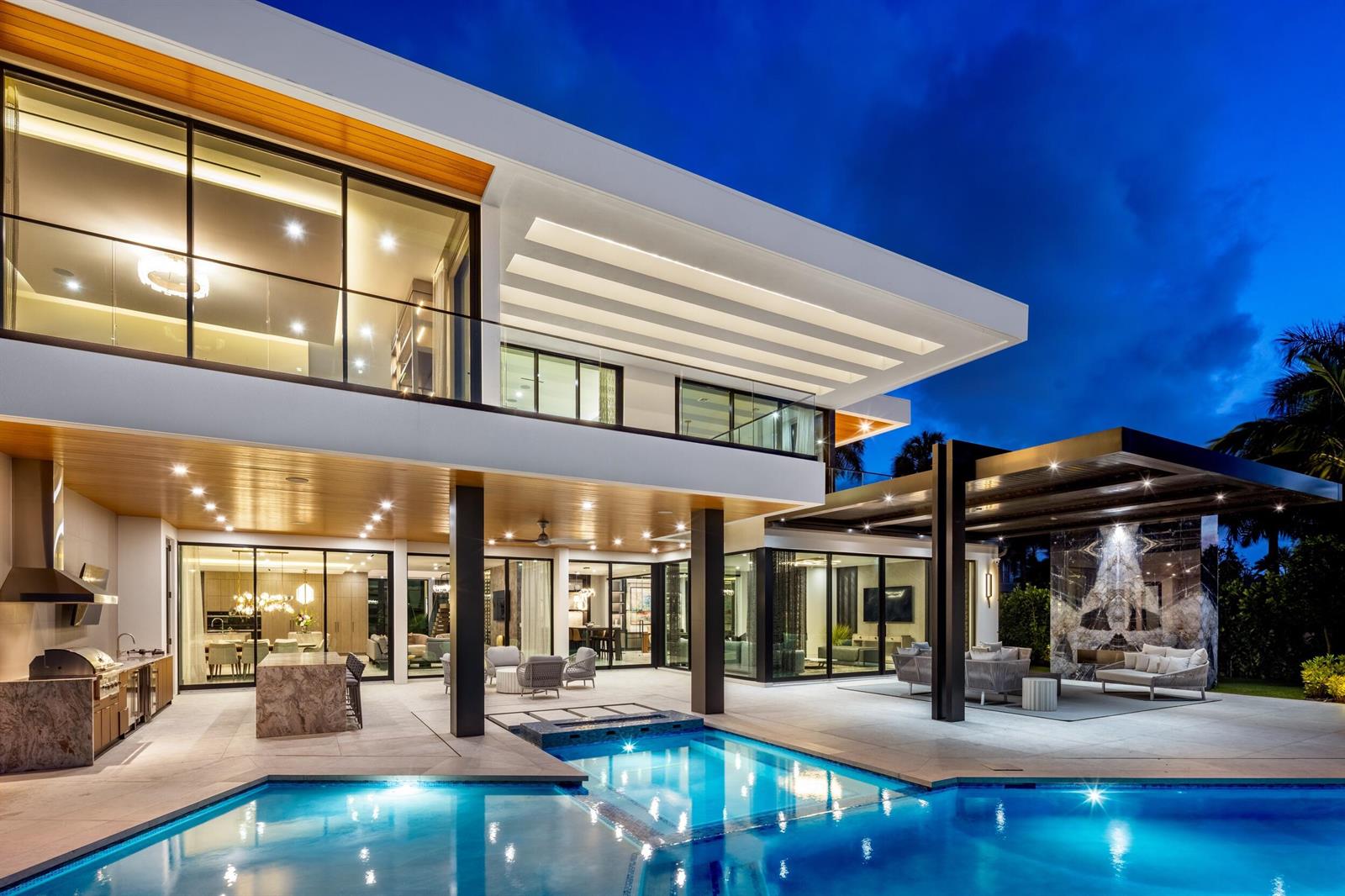 A modern two-story house with a pool, outdoor kitchen, and covered patio at twilight — 217 Thatch Palm Drive, Boca Raton FL 33432, BOCA RATON, FL