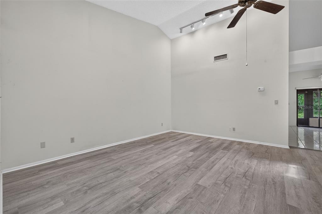 An empty living room with vaulted ceilings, light gray wood-look flooring, and a ceiling fan — 11754 SPRING TREE LANE, PORT RICHEY, FL