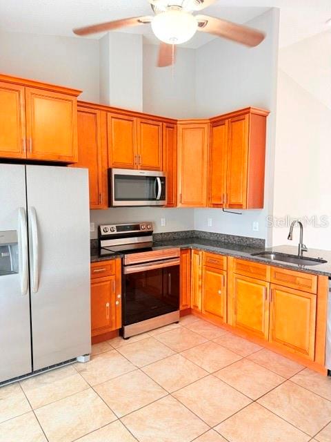 A kitchen features wood cabinets, stainless steel appliances, and tile flooring under a ceiling fan — 27 SLUMBER MEADOW TRAIL UNIT A, PALM COAST, FL