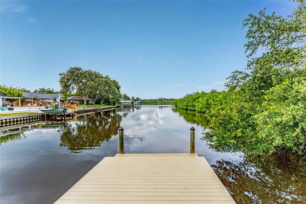 A wooden dock extends into a calm canal lined with trees and residential properties — 3225 ROSERY ROAD NE, LARGO, FL