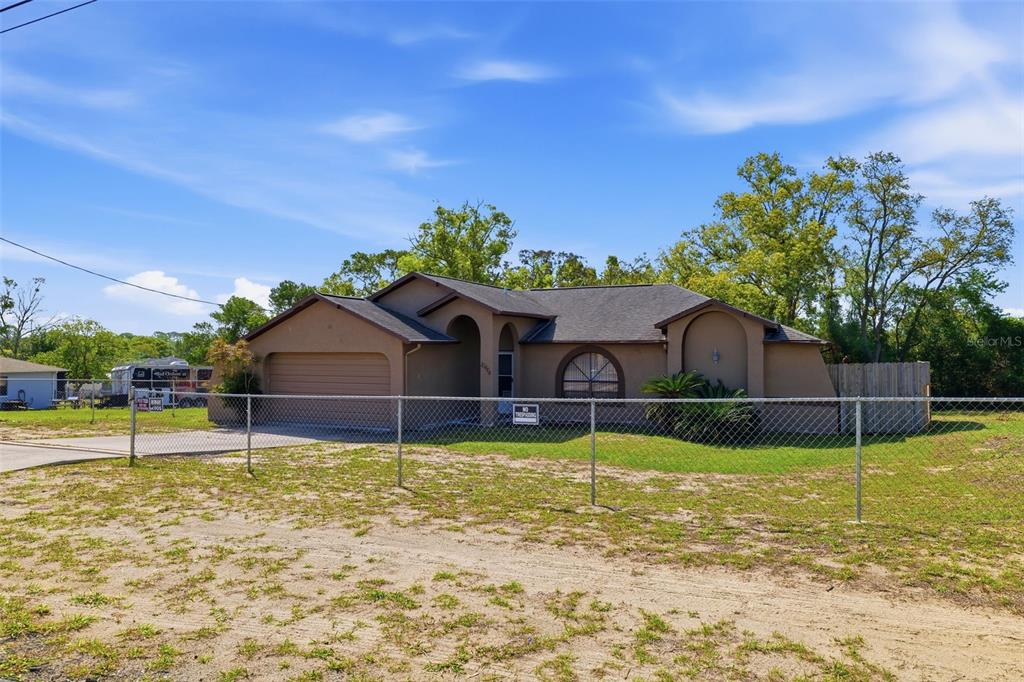 A single-story tan house with a garage and arched windows behind a chain-link fence — 10464 MADERIA STREET, SPRING HILL, FL