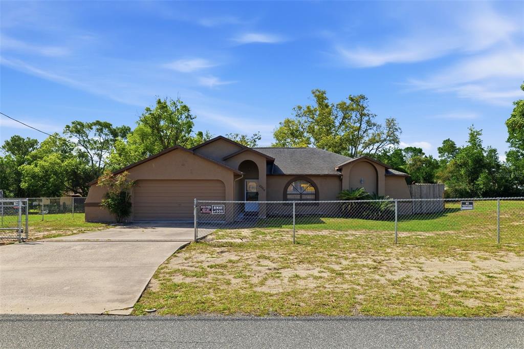 A single-story house with a tan stucco exterior and a chain-link fence in front — 10464 MADERIA STREET, SPRING HILL, FL