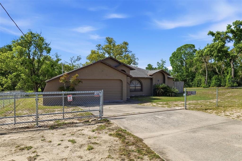 A tan single-story house with a two-car garage and a chain-link fence in the front — 10464 MADERIA STREET, SPRING HILL, FL
