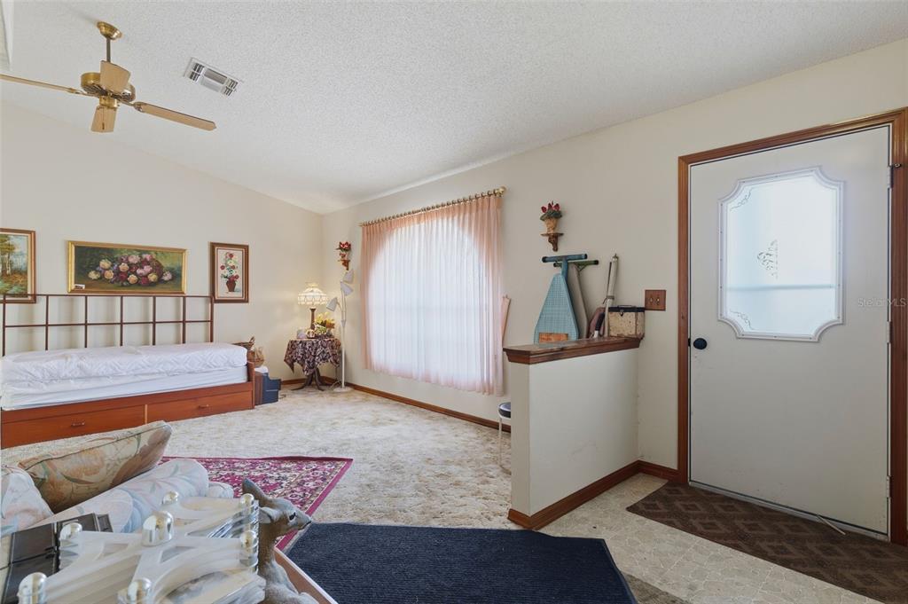 A living room features a daybed, carpeted flooring, a ceiling fan, and an entryway door — 10464 MADERIA STREET, SPRING HILL, FL