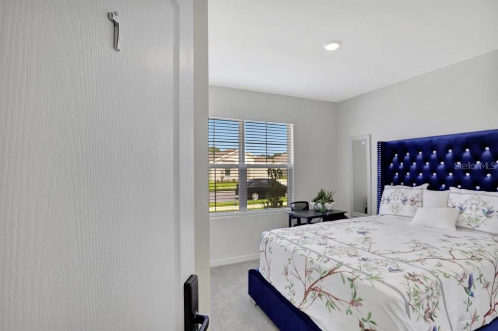 A bedroom features a blue tufted headboard, a floral bedspread, and a window with blinds — 937 CATTLEMAN STREET, WINTER HAVEN, FL