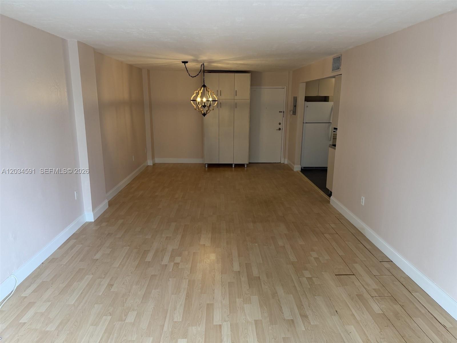 An empty living area features light wood-look flooring, beige walls, and a central hanging light fixture — 13120 SW 92nd Ave # 404, Miami FL 33176, MIAMI, FL