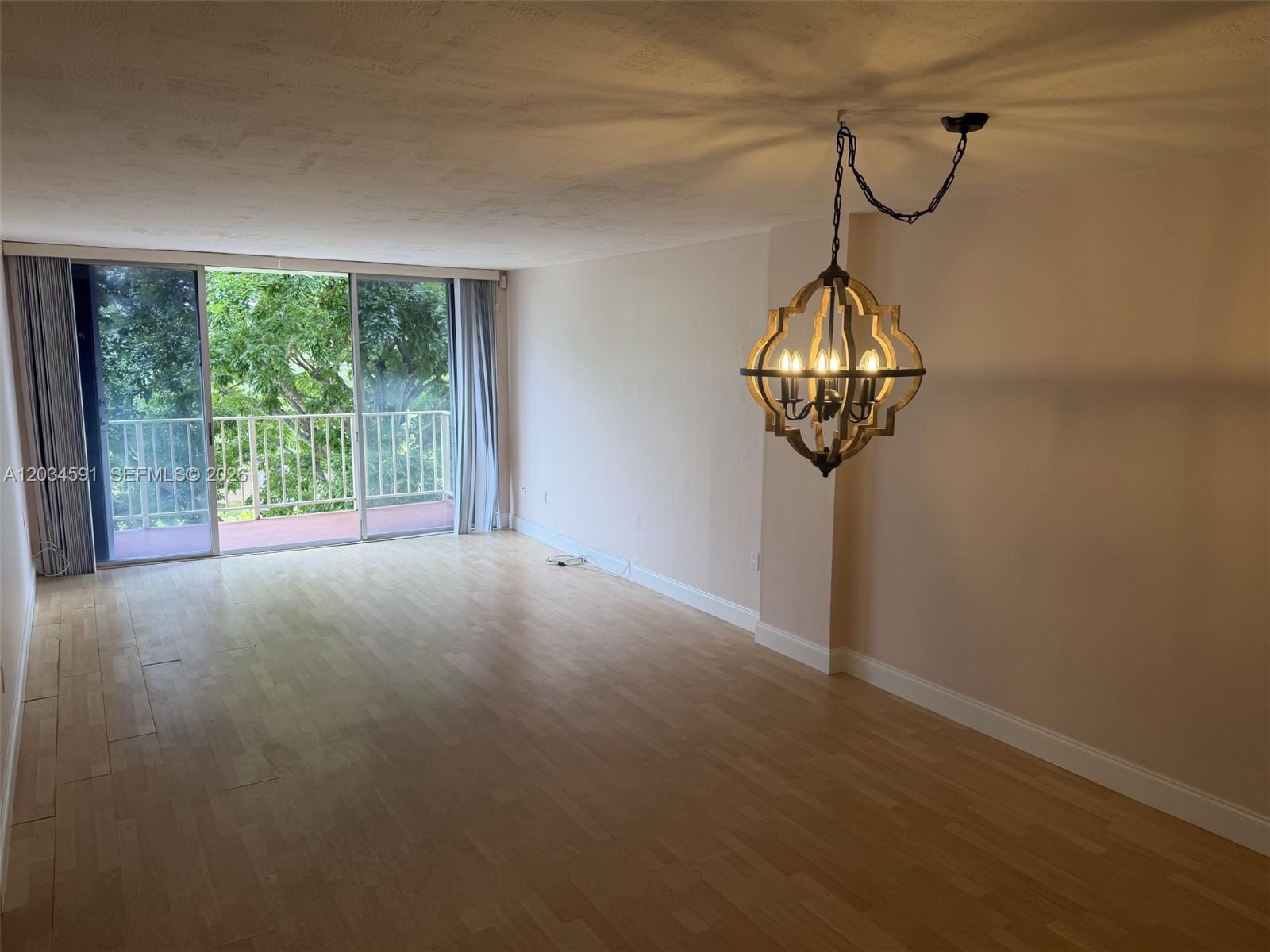 An empty living room features light wood flooring, a decorative chandelier, and a sliding glass door — 13120 SW 92nd Ave # 404, Miami FL 33176, MIAMI, FL
