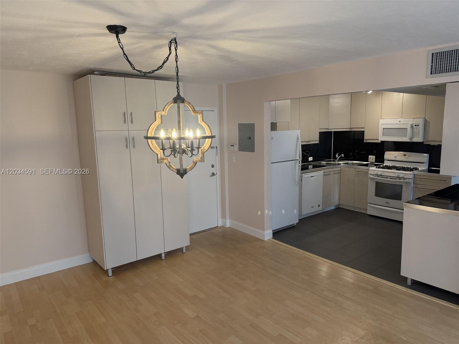 A dining area with a chandelier leads into a kitchen featuring white cabinets and appliances — 13120 SW 92nd Ave # 404, Miami FL 33176, MIAMI, FL