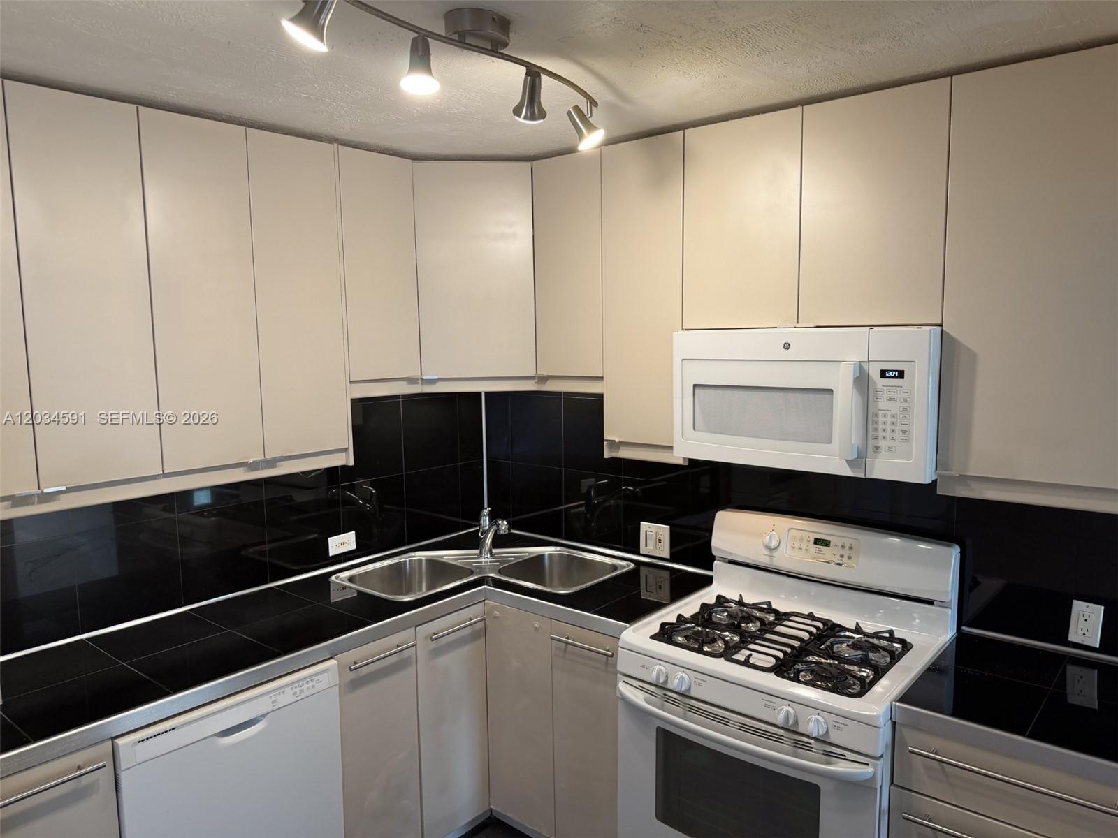 A kitchen features beige cabinets, black countertops, a corner sink, and white appliances — 13120 SW 92nd Ave # 404, Miami FL 33176, MIAMI, FL