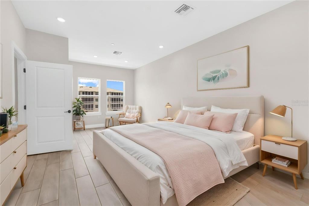 A bedroom features a light-colored bed, wood-look tile flooring, and two windows with exterior views — 1617 SEAHAVEN DRIVE UNIT 506, PUNTA GORDA, FL