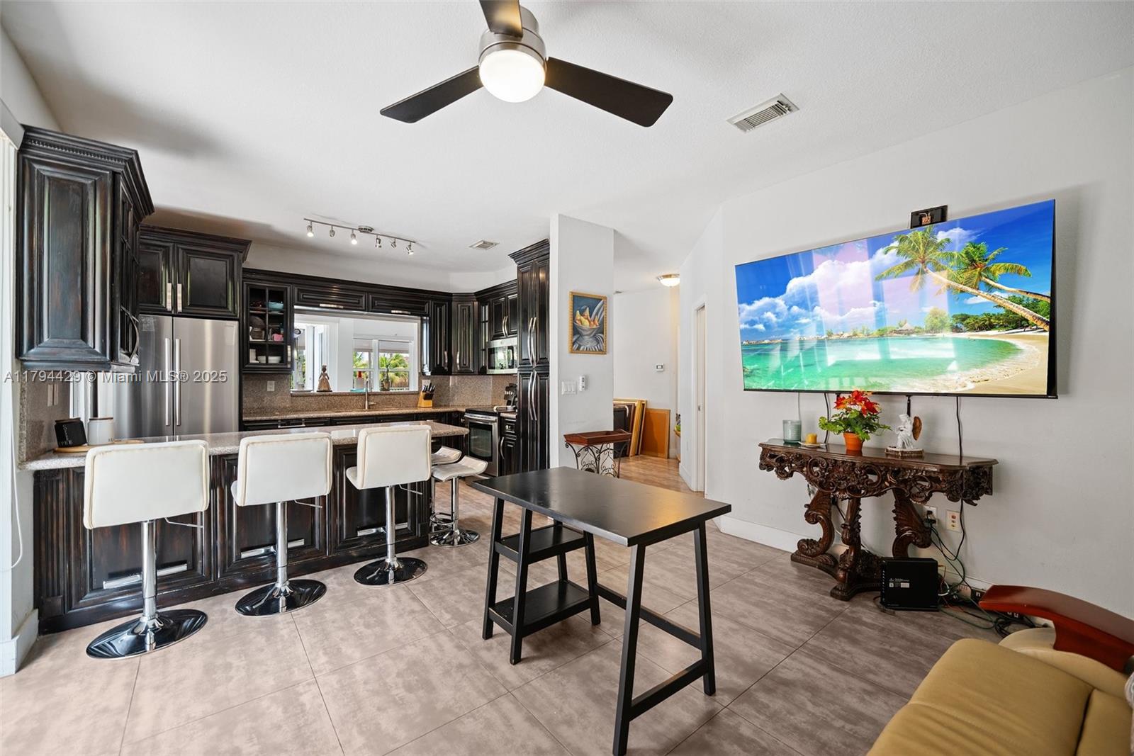 A kitchen with dark wood cabinets and a breakfast bar opens into a living area — 7045 SW 161 PL, Miami FL 33193, MIAMI, FL
