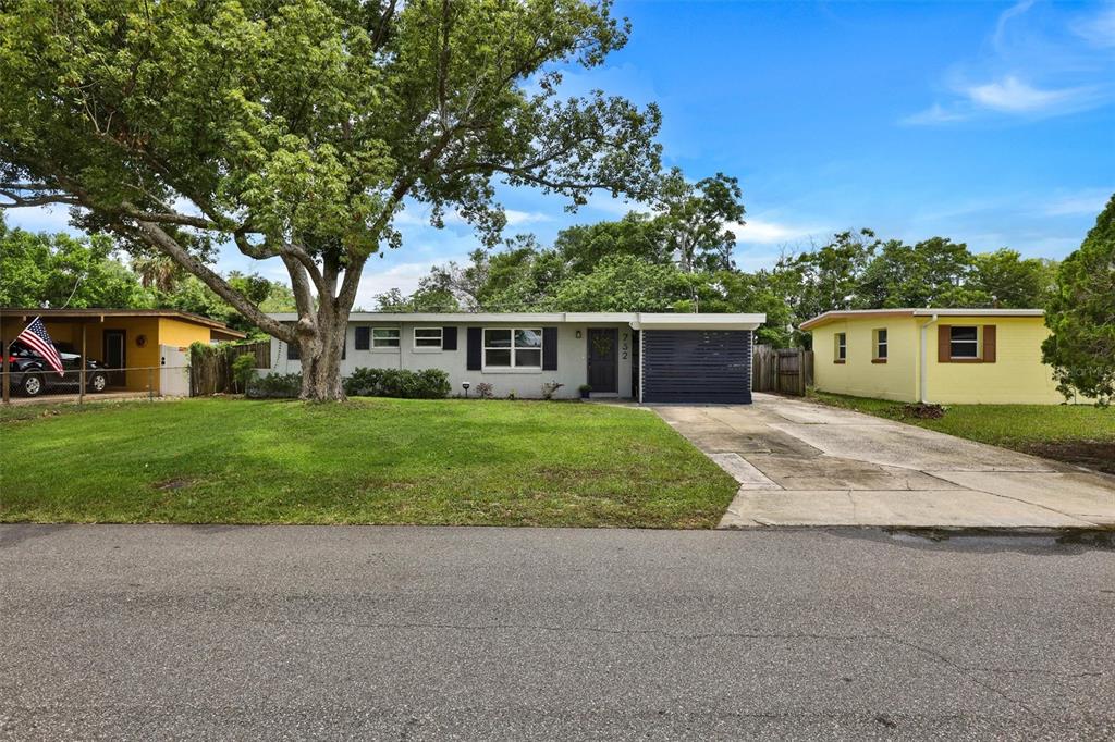 A single-story gray house with a dark garage door sits next to a yellow house — 732 LOGAN DRIVE, LONGWOOD, FL