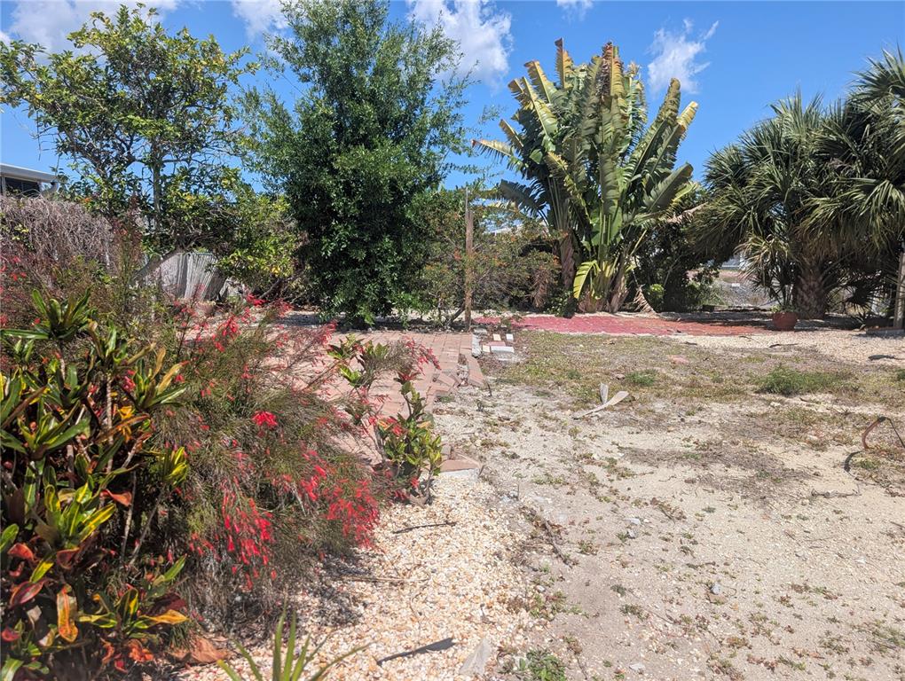 An outdoor yard features a brick patio area, various trees, shrubs, and sandy ground — 1273 KINGFISHER DRIVE, ENGLEWOOD, FL