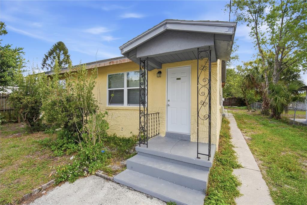 A yellow house exterior features a small covered porch with decorative iron supports and stairs — 8419 N SEMMES STREET, TAMPA, FL