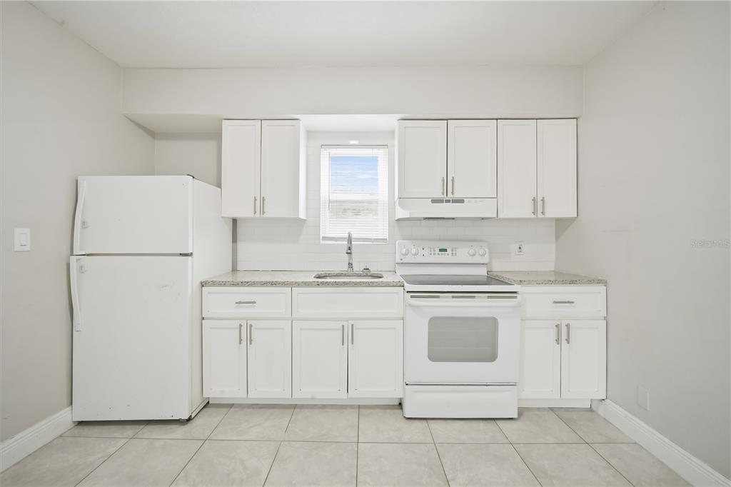 A kitchen features white cabinets, white appliances, a window, and light-colored tile flooring — 8419 N SEMMES STREET, TAMPA, FL