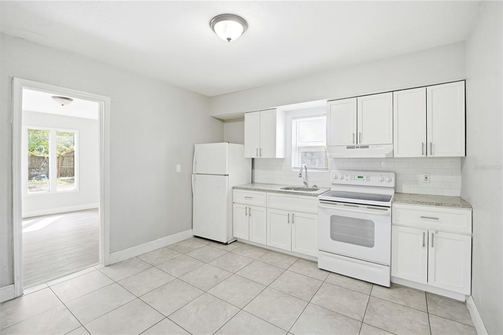 A kitchen with white cabinets, white appliances, light tile flooring, and a subway tile backsplash — 8419 N SEMMES STREET, TAMPA, FL