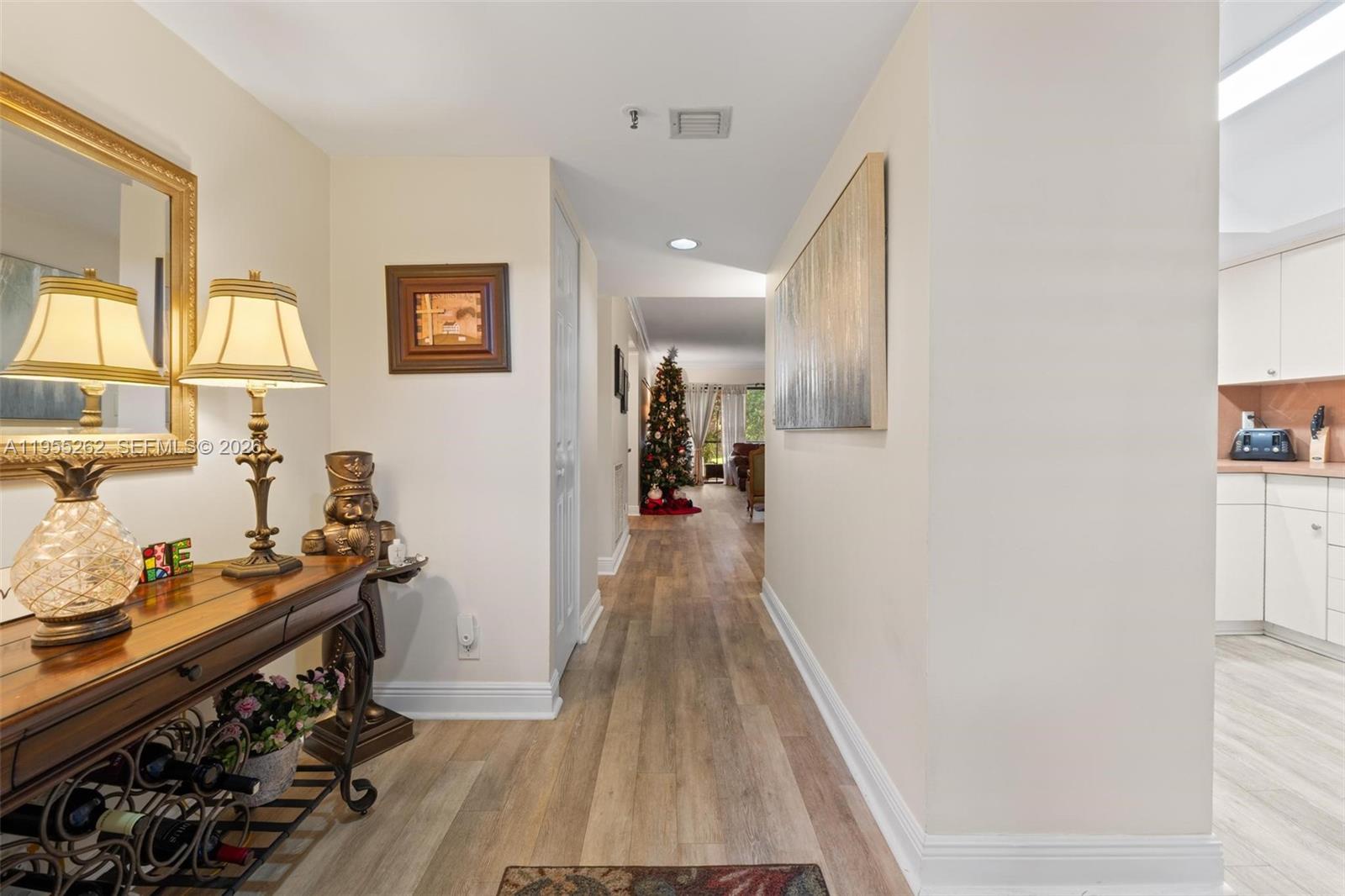 A hallway with wood-look flooring leads past a console table toward a decorated Christmas tree — 6662 Boca Del Mar Dr # 112, Boca Raton FL 33433, BOCA RATON, FL