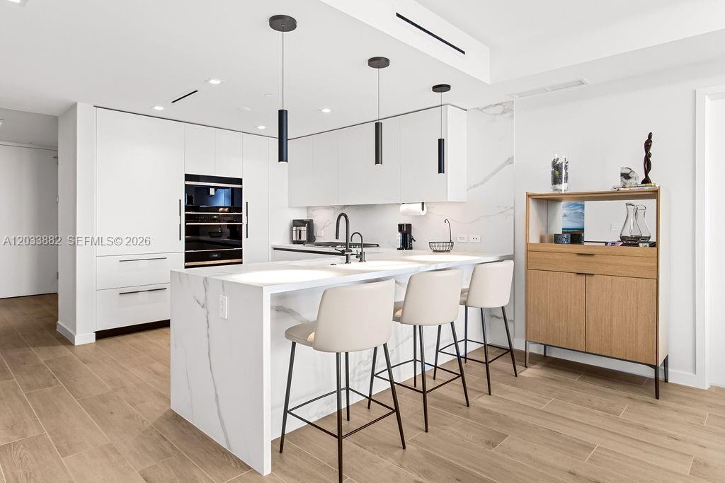 A modern kitchen features white cabinetry, a marble-topped island, and three bar stools — 1116 N Ocean Blvd # 1205, Pompano Beach FL 33062, POMPANO BEACH, FL
