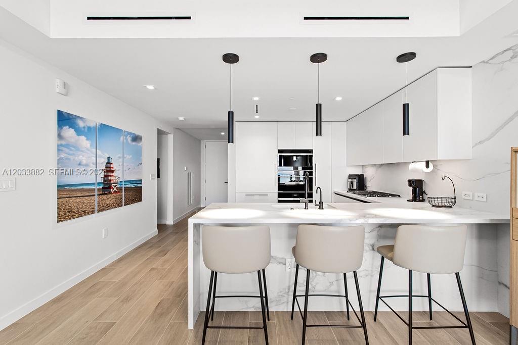 A modern kitchen features a marble-topped island with three stools and white cabinetry — 1116 N Ocean Blvd # 1205, Pompano Beach FL 33062, POMPANO BEACH, FL