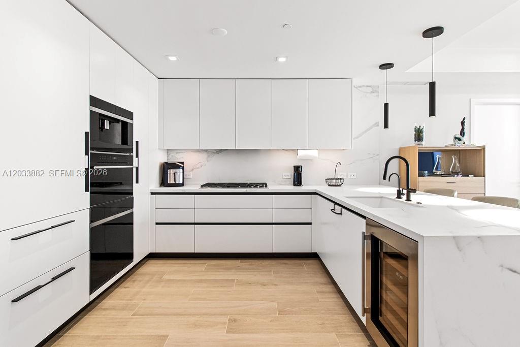 A modern kitchen features white flat-panel cabinetry, a marble-topped island, and light wood flooring — 1116 N Ocean Blvd # 1205, Pompano Beach FL 33062, POMPANO BEACH, FL