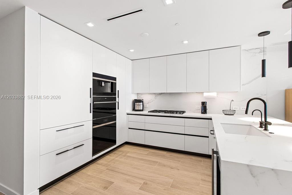 A modern kitchen features white flat-panel cabinetry, a marble backsplash, and a large island — 1116 N Ocean Blvd # 1205, Pompano Beach FL 33062, POMPANO BEACH, FL