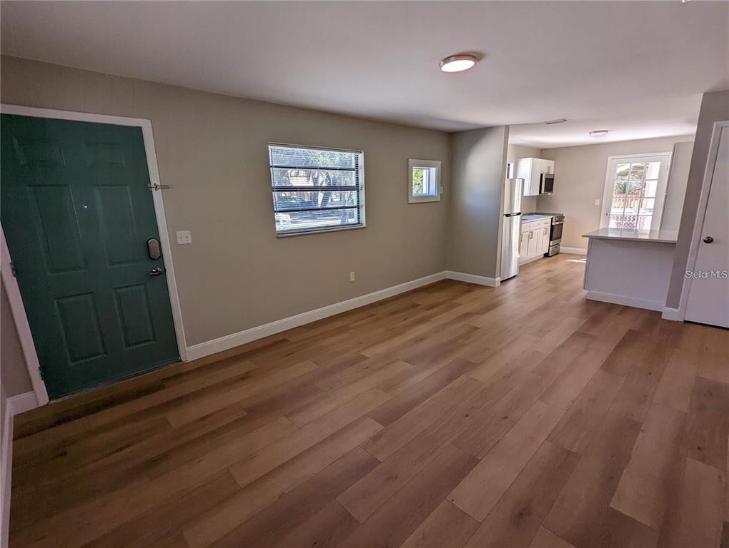An open-concept living area features light wood-look flooring, a teal front door, and a kitchen — 1920/1922 SPRINGTIME AVENUE, CLEARWATER, FL