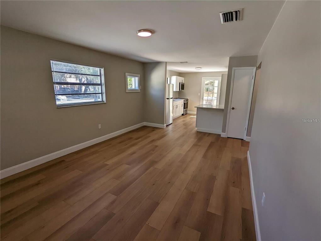 An open-concept living area features light wood flooring, neutral walls, and an adjacent kitchen — 1920/1922 SPRINGTIME AVENUE, CLEARWATER, FL
