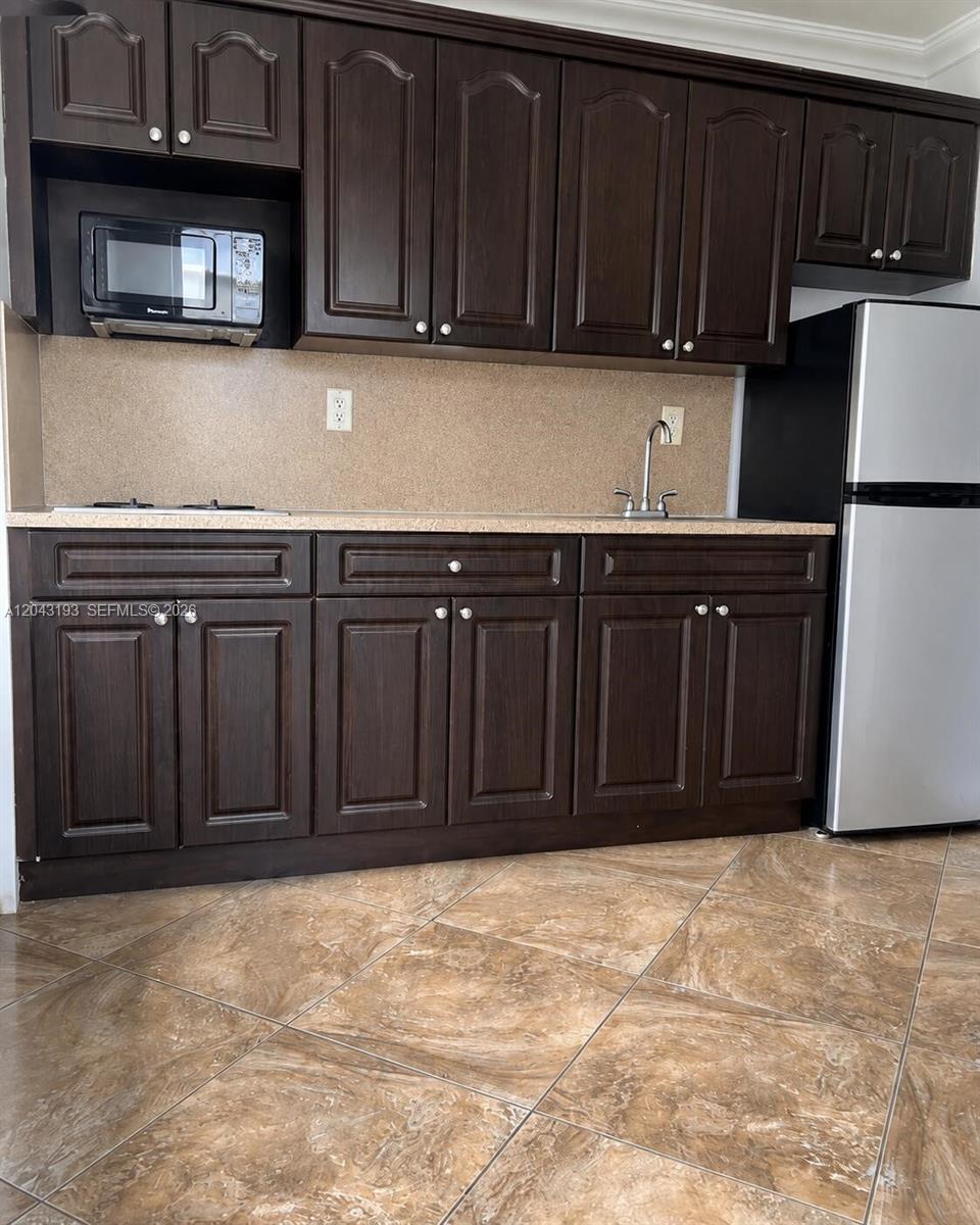 A kitchen features dark wood cabinets, a stainless steel refrigerator, and tan tile flooring — 18025 NW 83rd Ave # 1, Hialeah FL 33015, HIALEAH, FL