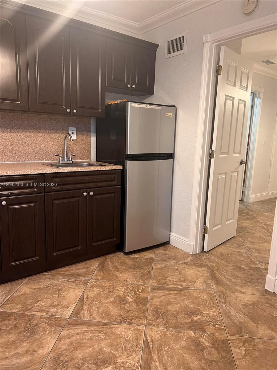 A small kitchen features dark wood cabinets, a stainless steel refrigerator, and tiled flooring — 18025 NW 83rd Ave # 1, Hialeah FL 33015, HIALEAH, FL