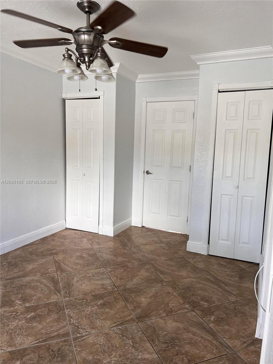 A room with brown tile flooring, a ceiling fan, and three white doors — 18025 NW 83rd Ave # 1, Hialeah FL 33015, HIALEAH, FL