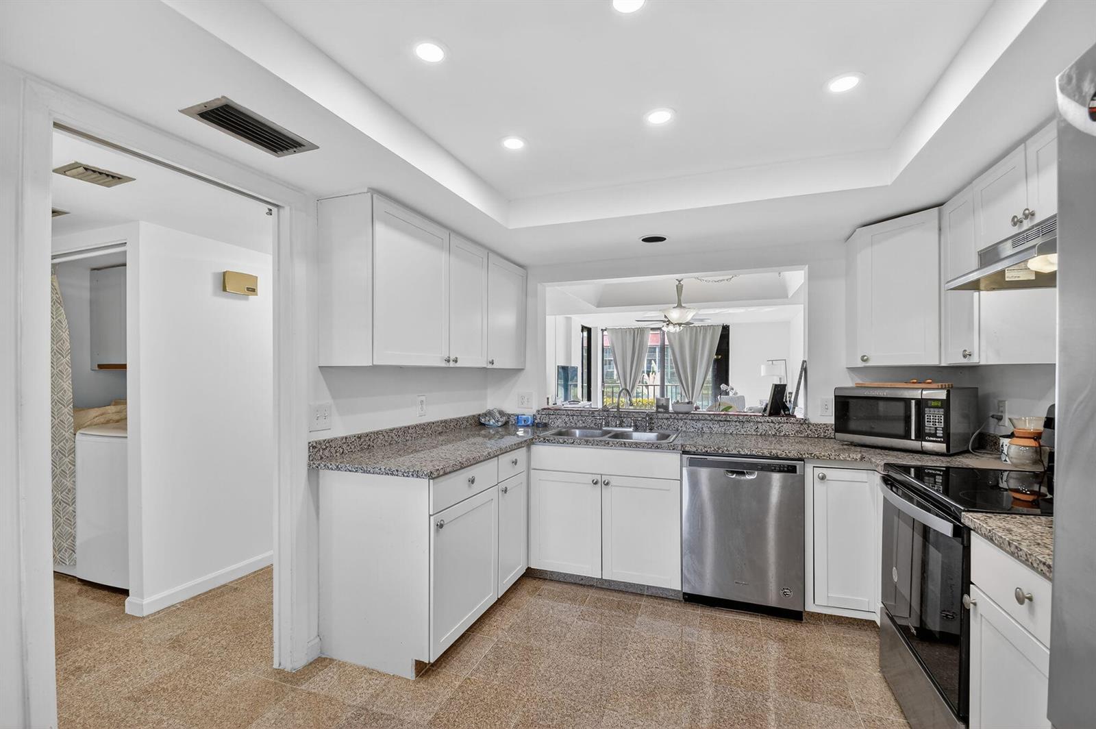 A kitchen features white cabinets, granite countertops, stainless steel appliances, and a pass-through window — 7030 Half Moon Circle # 117, Hypoluxo FL 33462, HYPOLUXO, FL