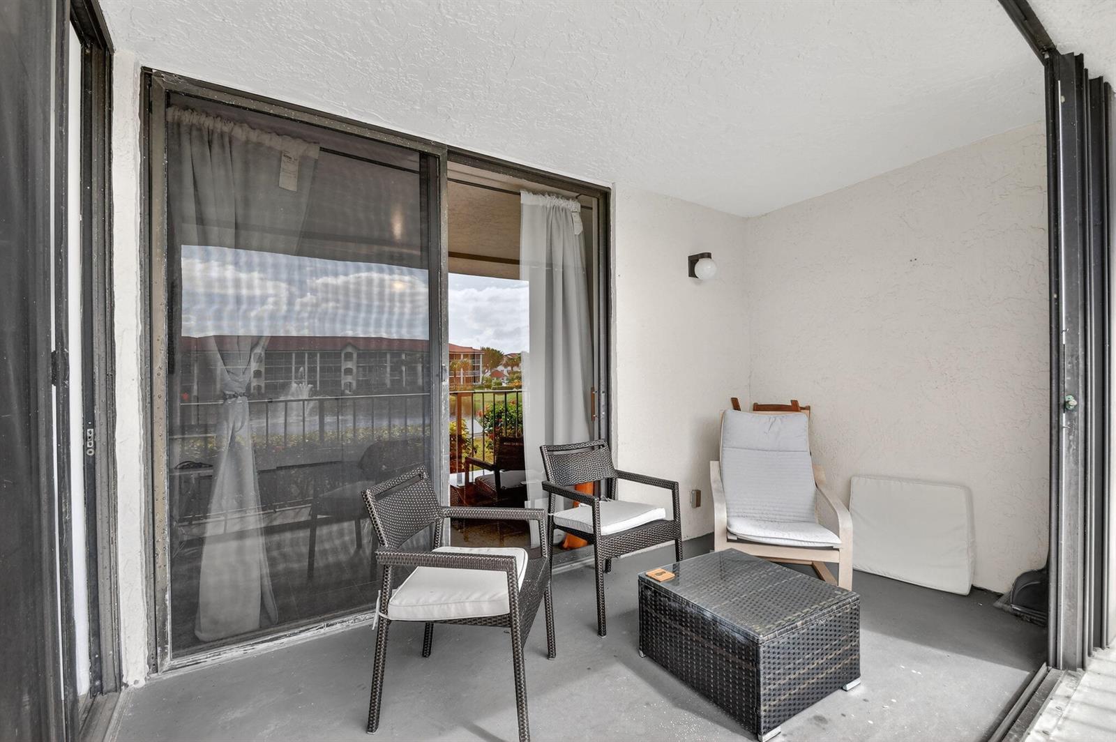 A covered balcony features a small coffee table, three chairs, and a sliding glass door — 7030 Half Moon Circle # 117, Hypoluxo FL 33462, HYPOLUXO, FL