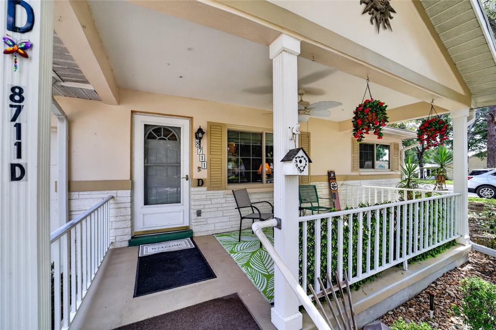 A covered front porch features a white railing, a welcome mat, and hanging flower baskets — 8711 SW 96TH LANE UNIT D, OCALA, FL