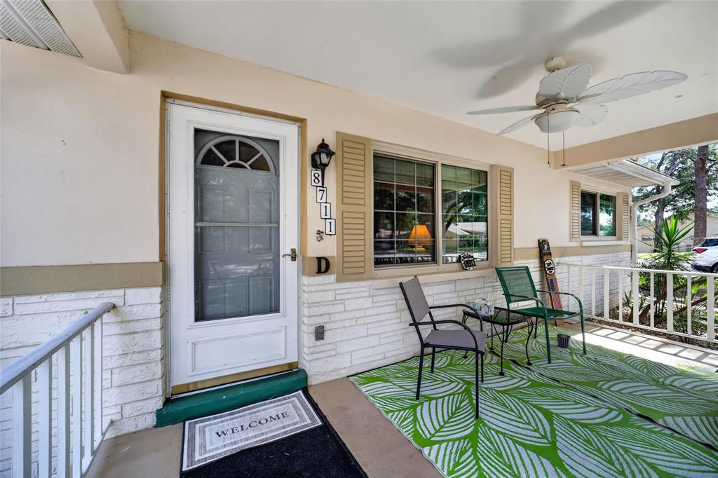 A covered front porch features a white door, stone siding, a ceiling fan, and furniture — 8711 SW 96TH LANE UNIT D, OCALA, FL
