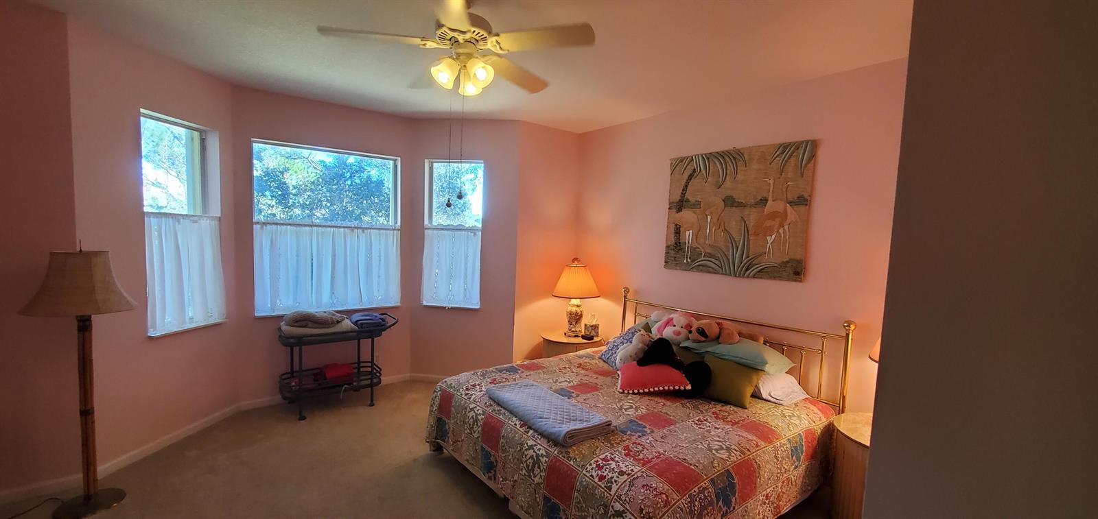 A bedroom with pink walls, a brass bed frame, and a ceiling fan — 1128 NW Mossy Oak Way, Jensen Beach FL 34957, JENSEN BEACH, FL