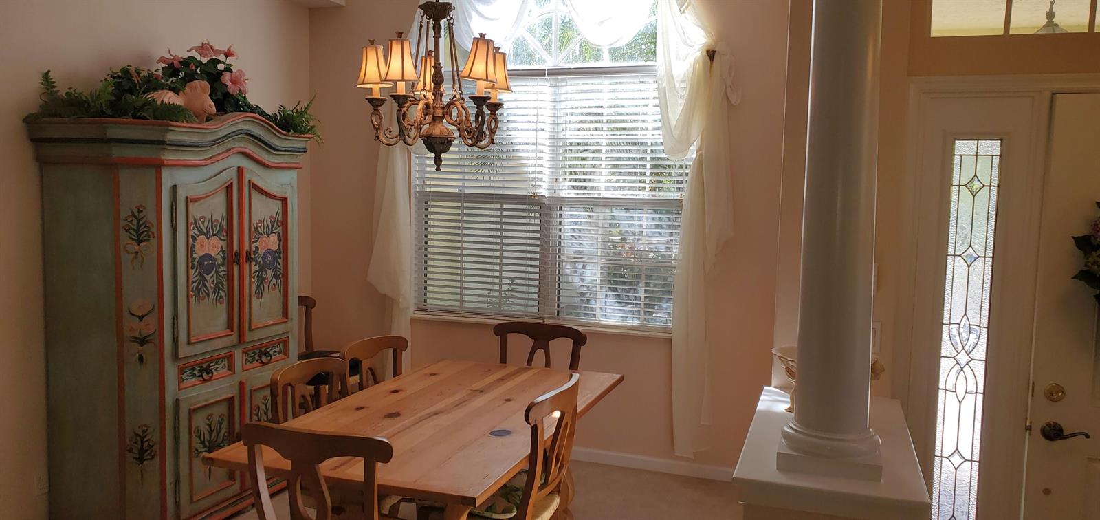 A dining room features a wooden table, a painted cabinet, and a chandelier near a window — 1128 NW Mossy Oak Way, Jensen Beach FL 34957, JENSEN BEACH, FL