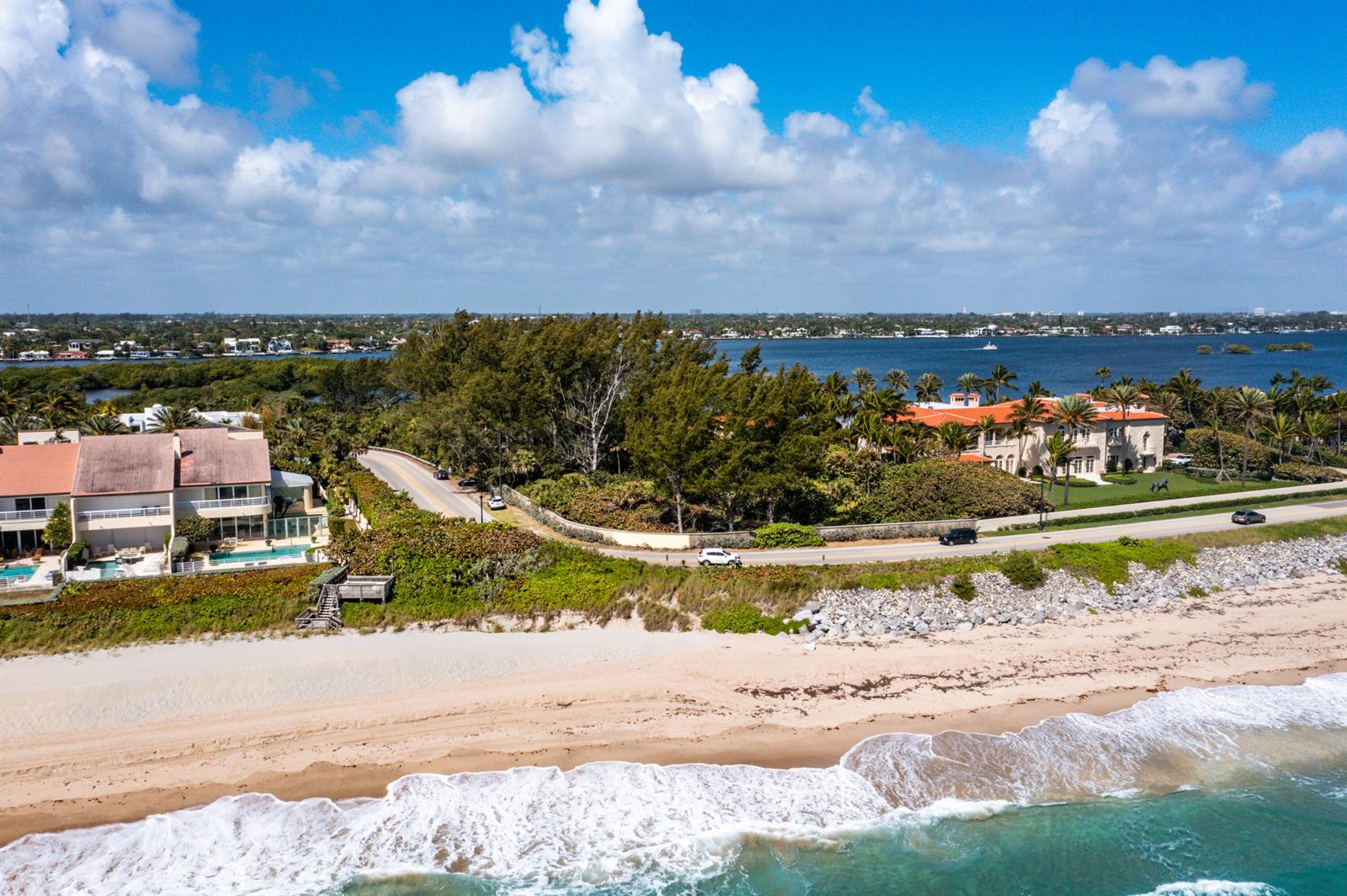 An aerial view shows a coastal road separating a sandy beach from luxury waterfront homes — 1980 S Ocean Boulevard, Palm Beach FL 33480, PALM BEACH, FL