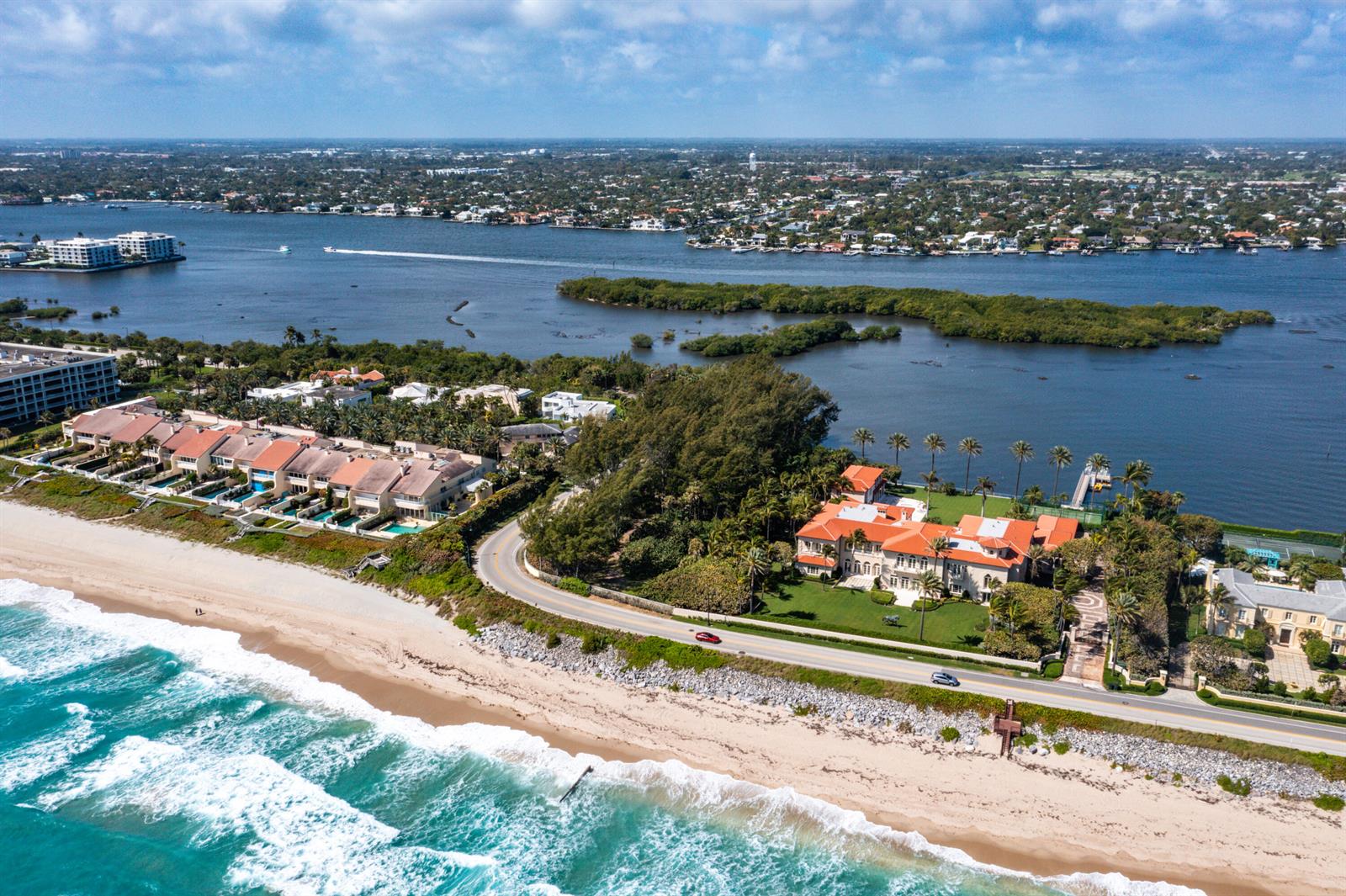 An aerial view shows a large waterfront estate with a red roof beside a beach — 1980 S Ocean Boulevard, Palm Beach FL 33480, PALM BEACH, FL