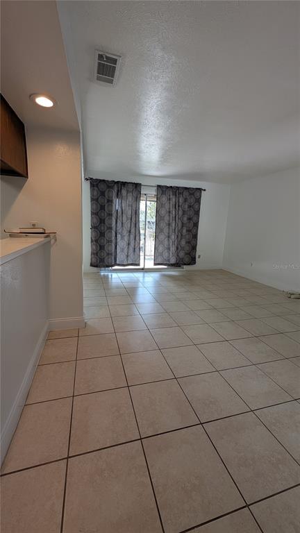 A living room with light-colored tile flooring and sliding glass doors covered by patterned curtains — 4028 BILLINGSGATE RD, ORLANDO, FL