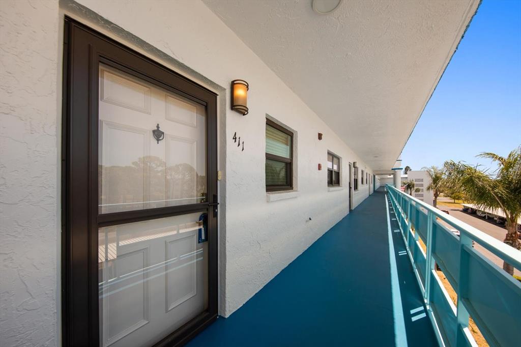 An exterior walkway with blue flooring leads past apartment doors and a metal railing — 5970 80TH STREET N UNIT 411, ST PETERSBURG, FL