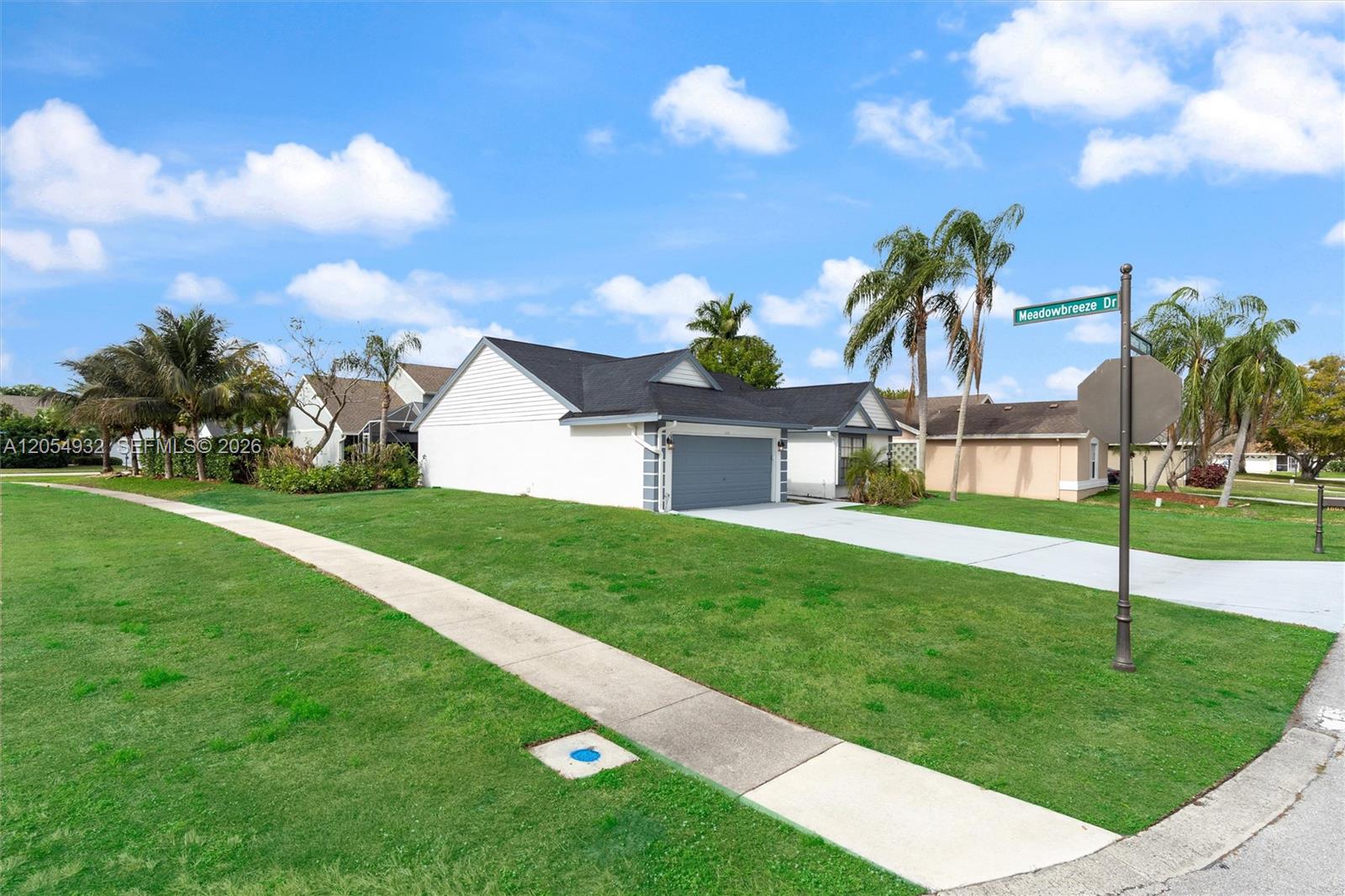 A single-story house with a white exterior and gray garage sits on a corner lot — 1665 Weather Vane Pl, Wellington FL 33414, WELLINGTON, FL