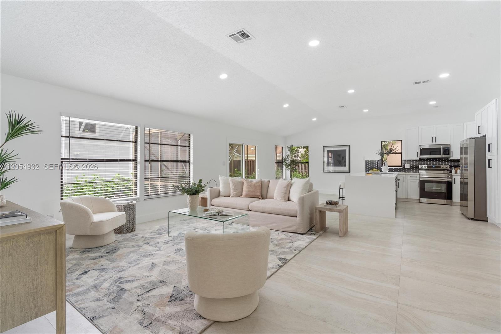 An open-concept living room and kitchen feature light tile floors, white walls, and neutral furniture — 1665 Weather Vane Pl, Wellington FL 33414, WELLINGTON, FL