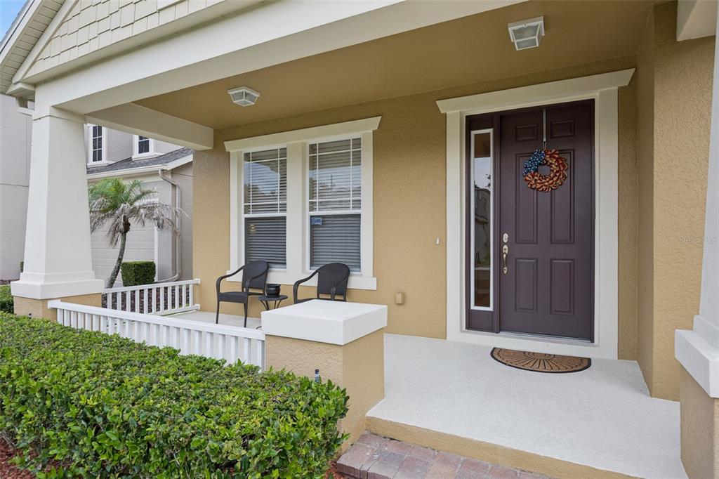 A covered front porch with a dark door, two chairs, and a white railing — 11942 SHELTERING PINE DRIVE, ORLANDO, FL