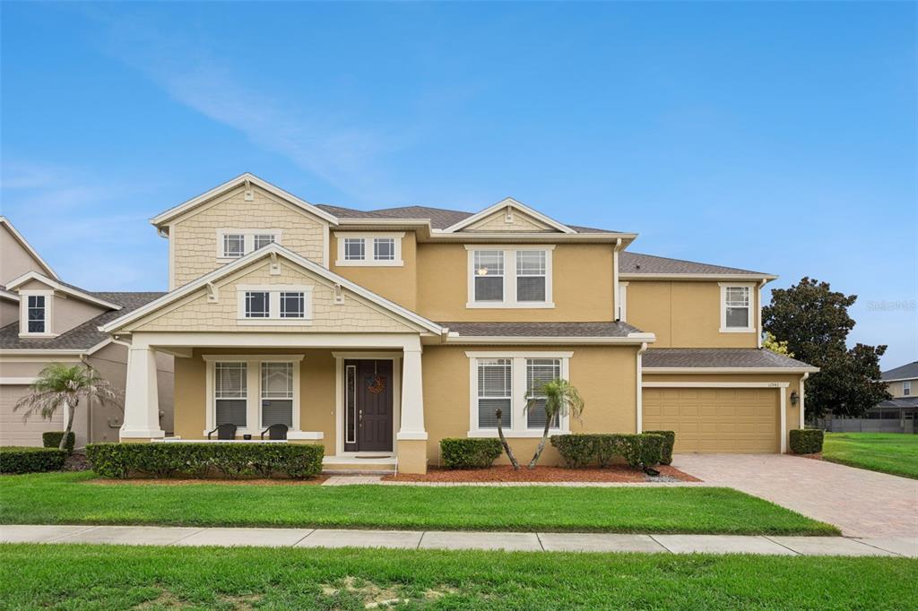 A two-story tan house with a front porch, a two-car garage, and a lawn — 11942 SHELTERING PINE DRIVE, ORLANDO, FL