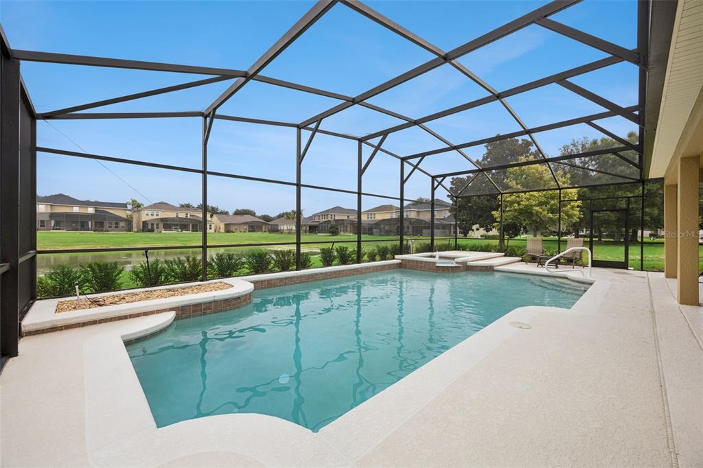 A screened-in swimming pool with a spa overlooks a pond and neighboring houses — 11942 SHELTERING PINE DRIVE, ORLANDO, FL
