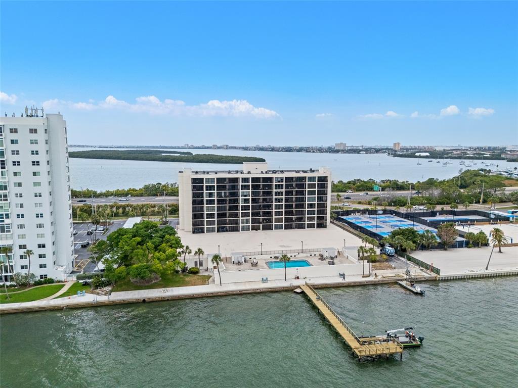 An aerial view shows a waterfront condominium building with a pool, tennis courts, and dock — 7100 SUNSHINE SKYWAY LANE S UNIT 701, ST PETERSBURG, FL