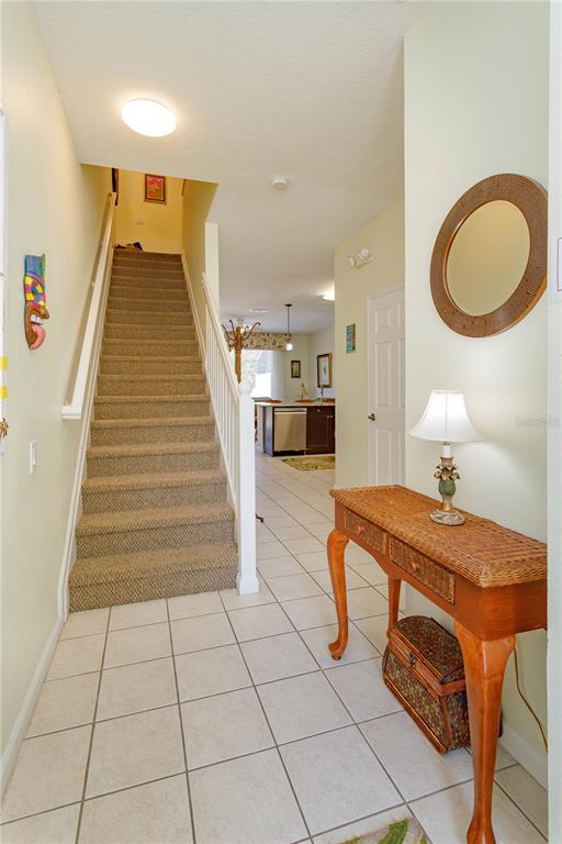A tiled entryway features a carpeted staircase with a white railing and a wicker console table — 2348 SILVER PALM DRIVE, KISSIMMEE, FL