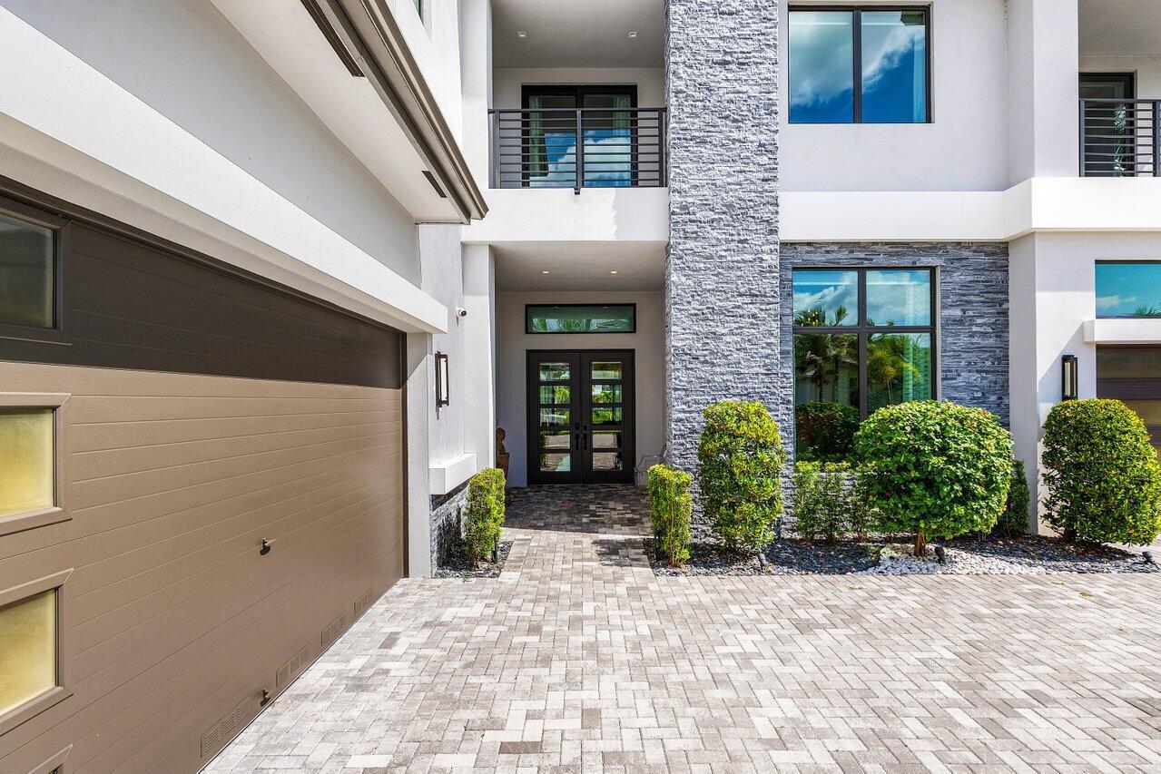 The exterior of a modern home features a stone facade, paved driveway, and double front doors — 9625 Vescovato Way, Boca Raton FL 33496, BOCA RATON, FL