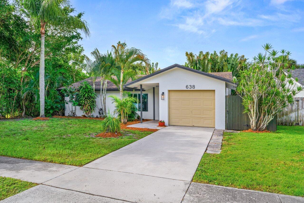A single-story house with a white exterior, a tan garage door, and lush tropical landscaping — 638 SW 4th Avenue, Boynton Beach FL 33426, BOYNTON BEACH, FL