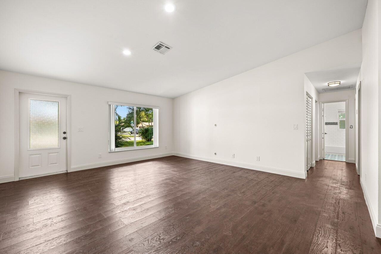 A bright, empty living room features white walls, dark wood-look flooring, and a glass-paneled door — 638 SW 4th Avenue, Boynton Beach FL 33426, BOYNTON BEACH, FL
